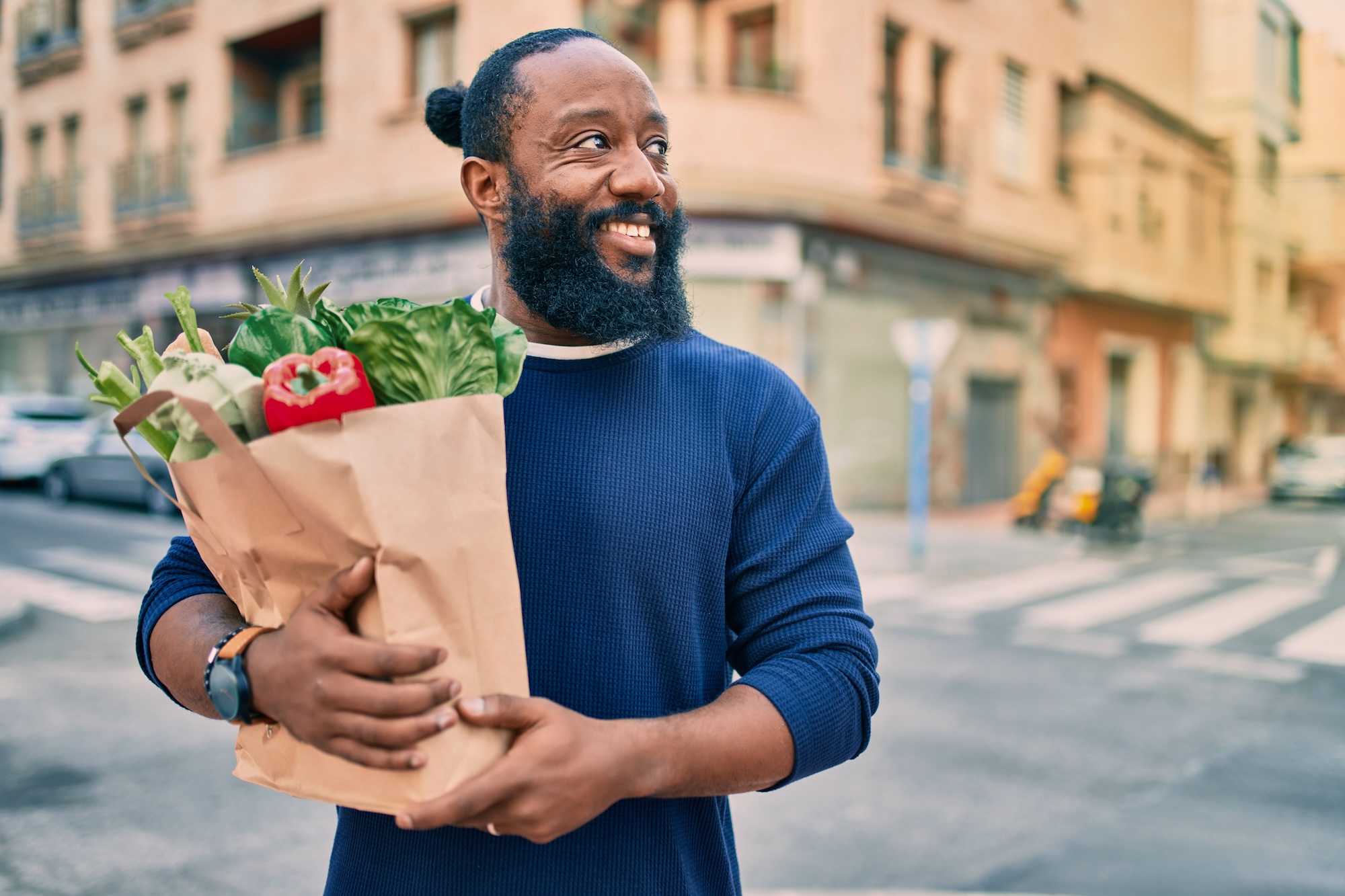 A man smiling and holding a bag of groceries