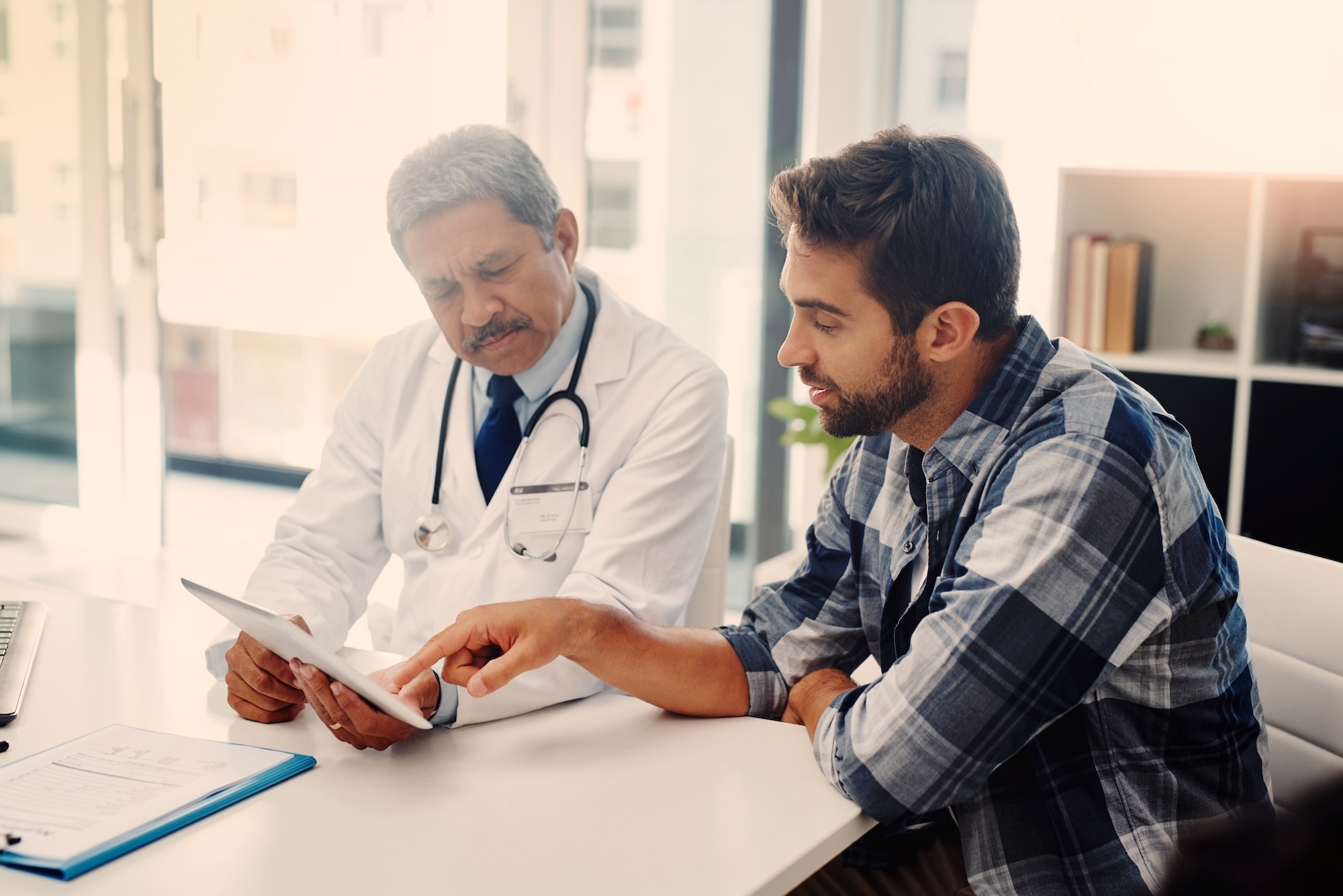 A doctor holding a tablet while the patient speaks to him and points to it